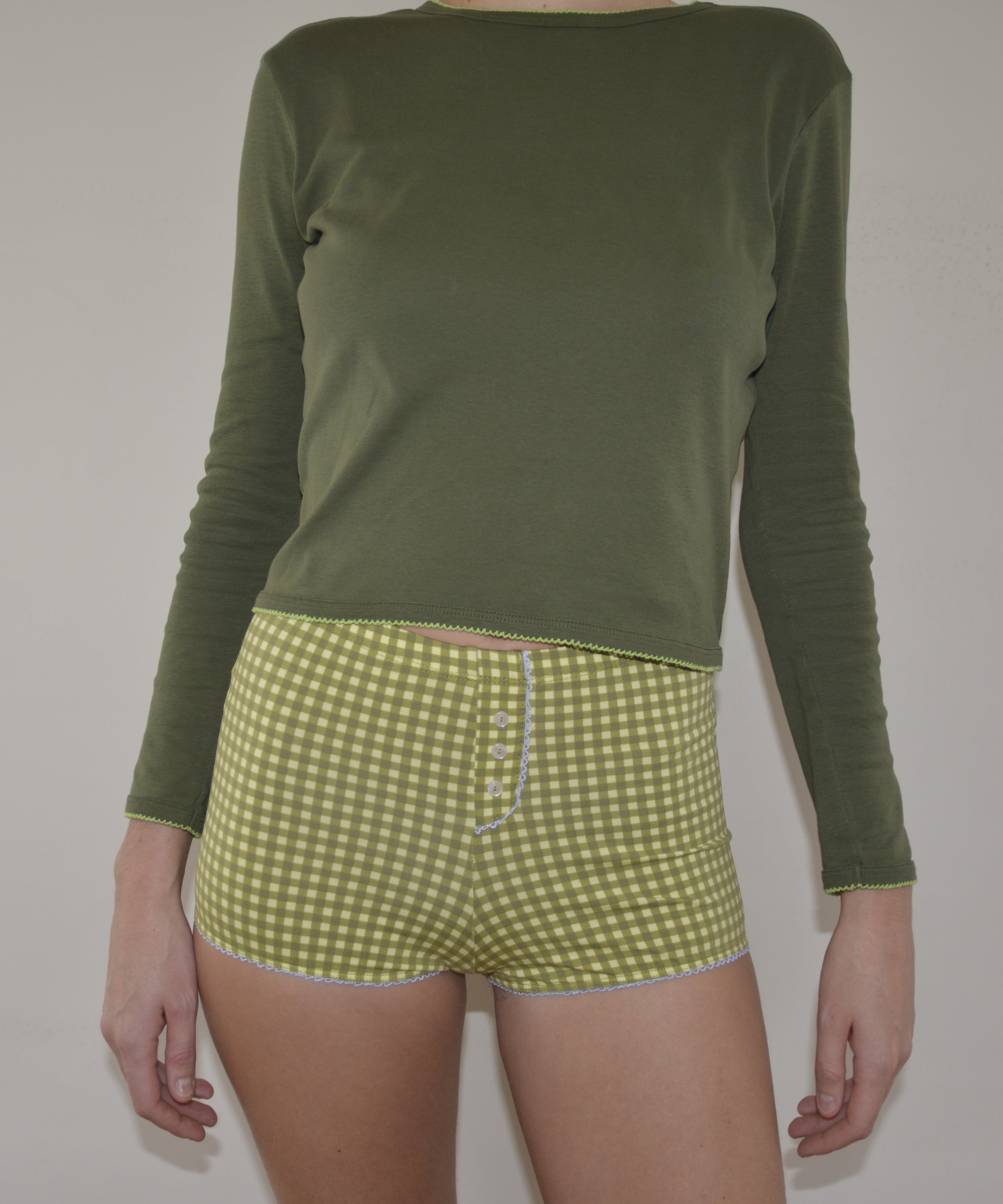 Person wearing a green long-sleeve shirt and green checkered shorts on a plain background